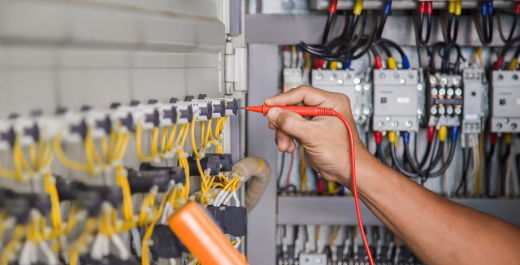 A commercial electrician performing electrical maintenance on a control panel with a multimeter tester in a professional setting