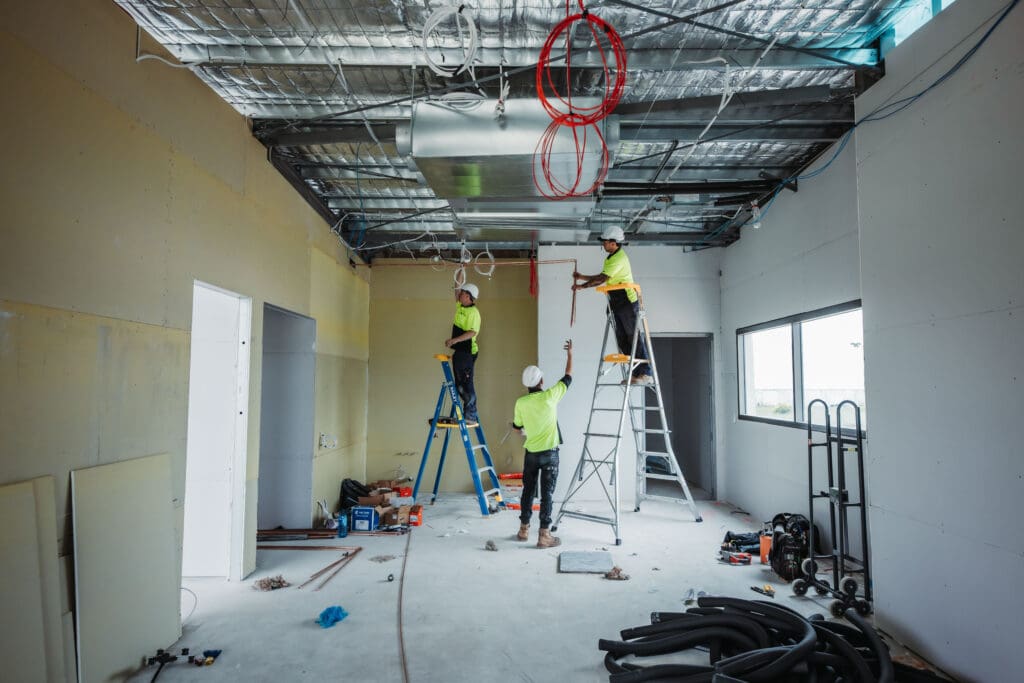 Two strata electricians from DCEA on a ladder, expertly installing ceiling wires in a commercial building