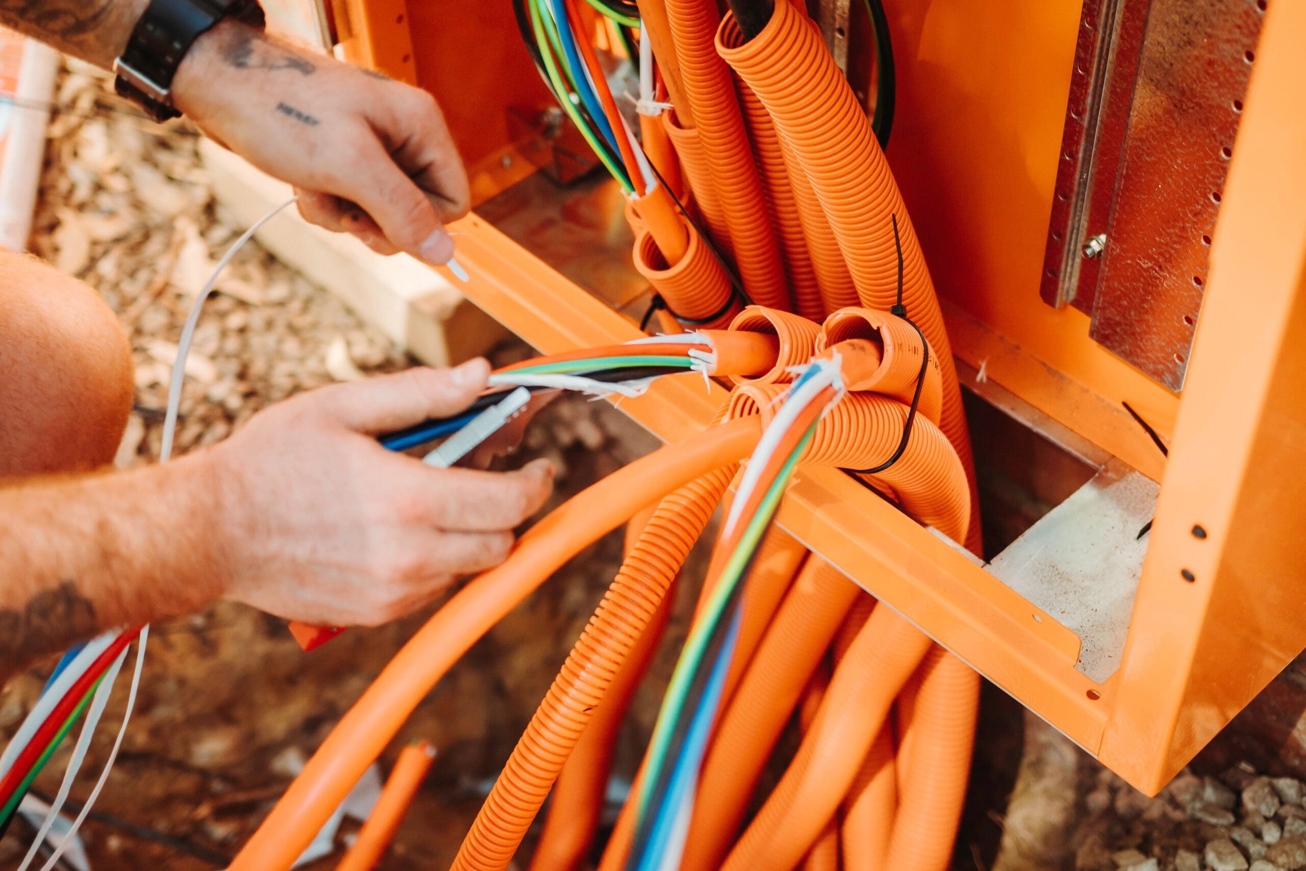 A commercial electrician in Perth is engaged in maintenance on an orange electrical box